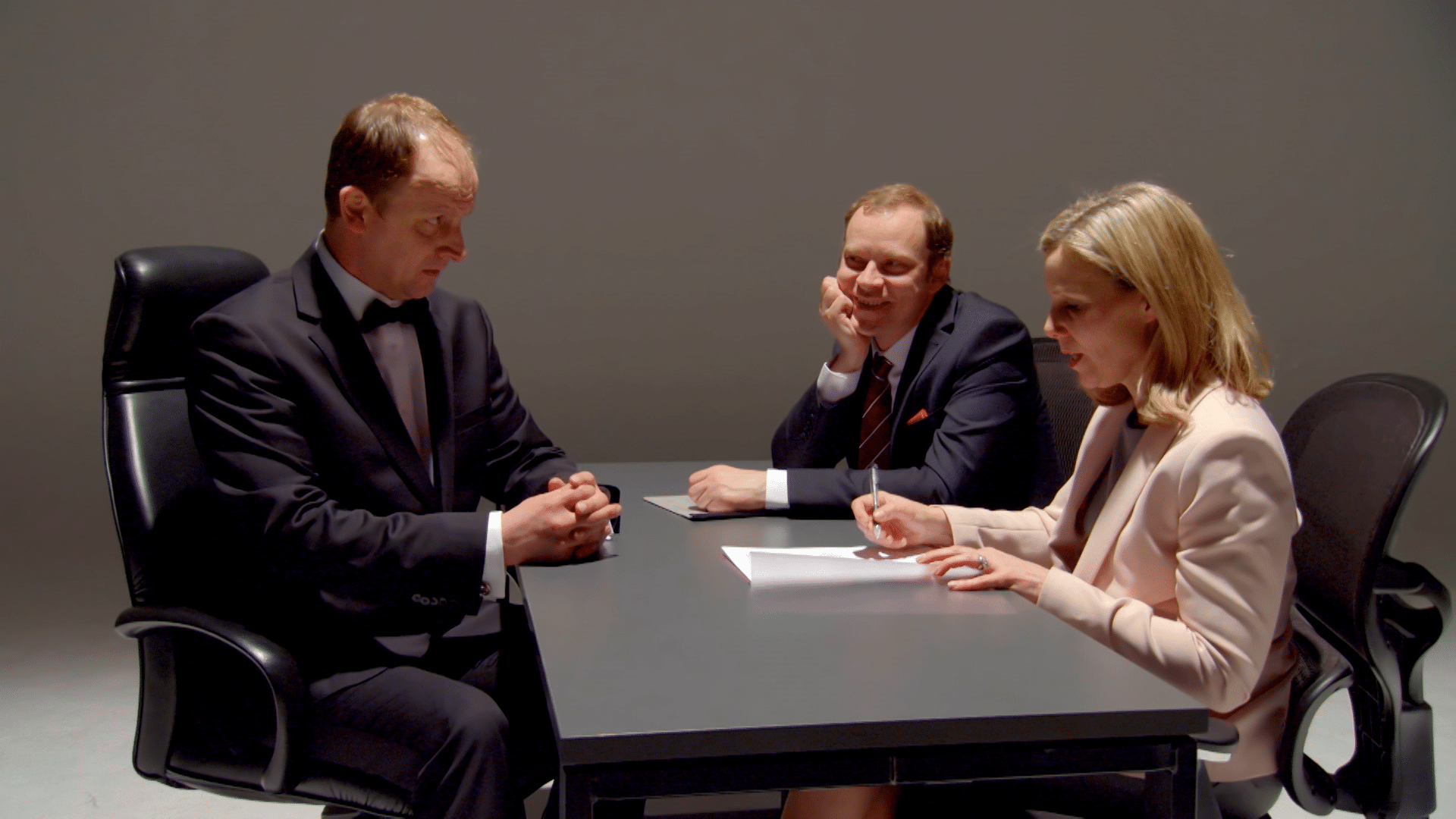 Two men and a woman sitting in a dark room at a table.