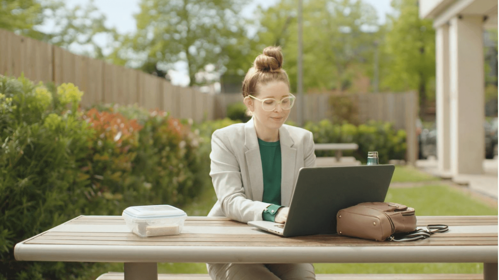 A woman sat outside at a picnic table on her laptop working.