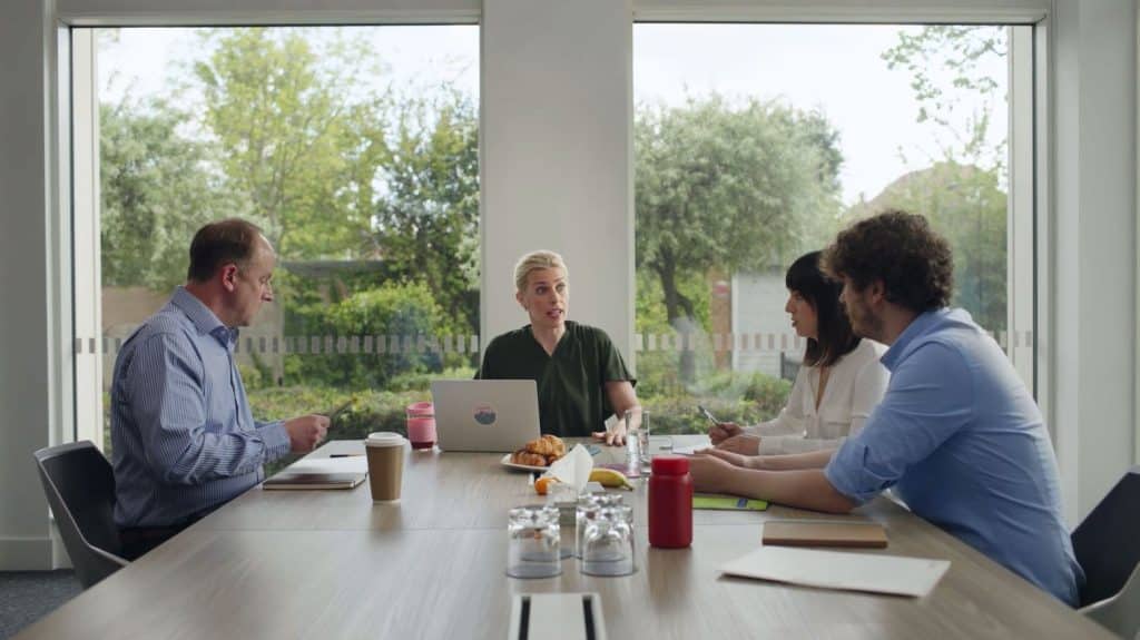 Four people sat in a room at a table having a meeting.