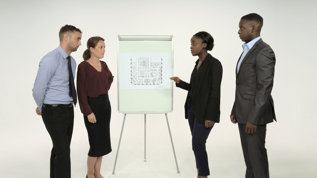 Four people standing around whiteboard looking at one another.