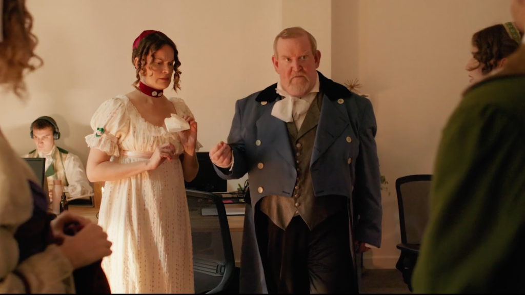 Man and Woman in periodic clothing in a room with others surrounding.