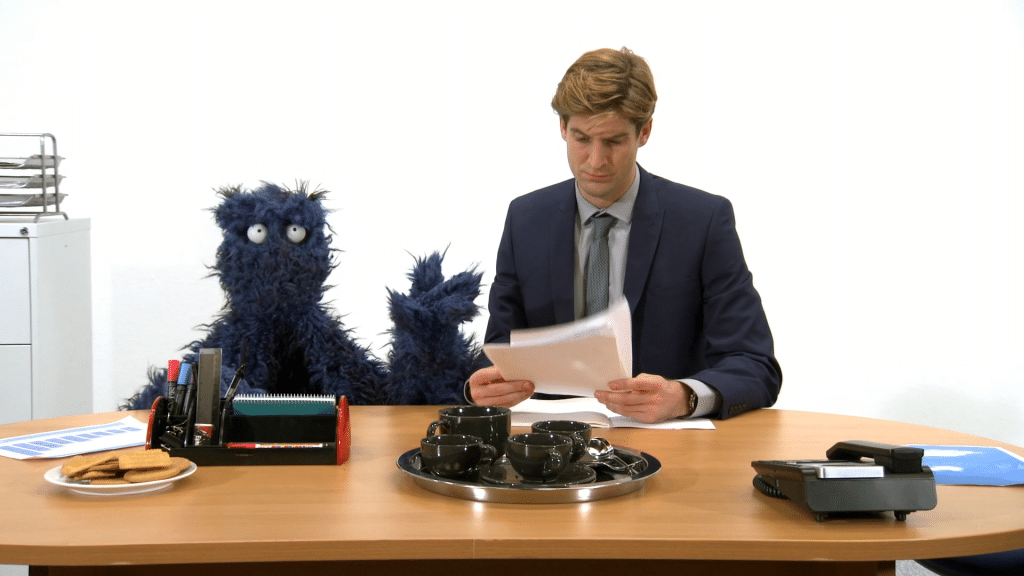 Man looking at papers at a desk next to a monster.