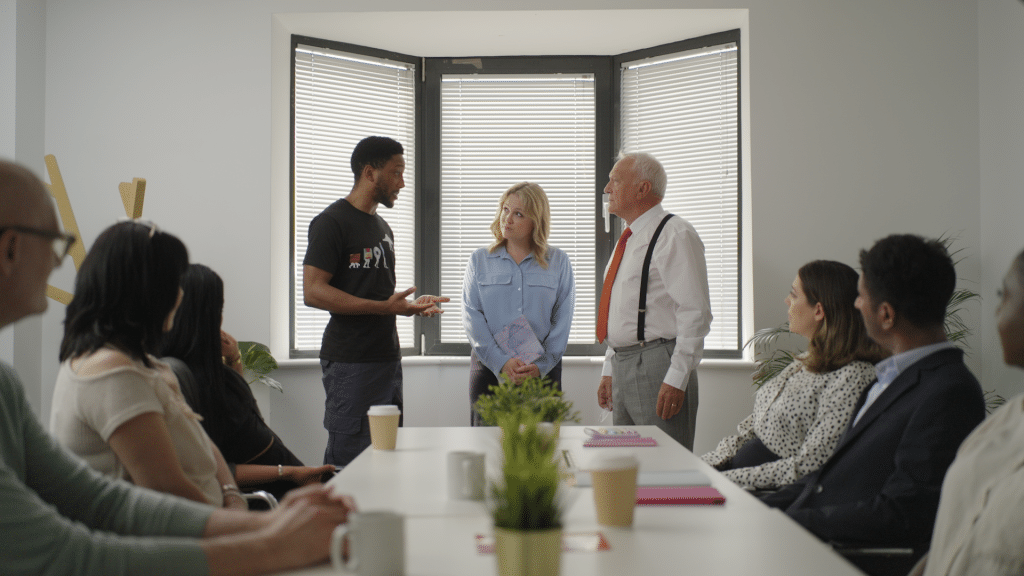 Group of people in a meeting room with some of them standing up at the end of the table