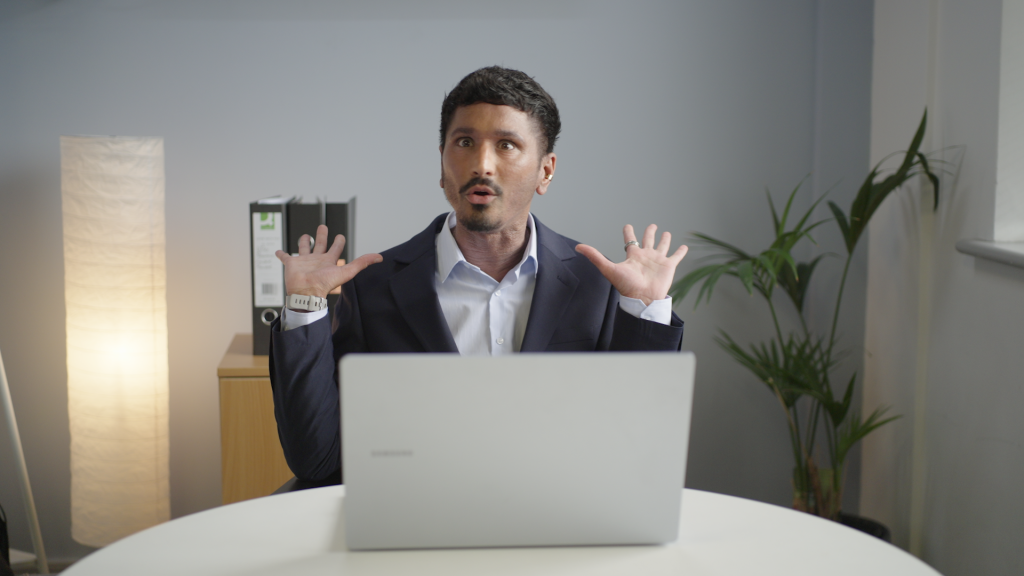 Man defensively putting up his hands behind a laptop