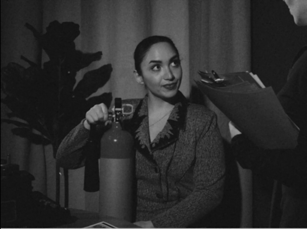 A black and white image of a woman sat with a fire extinguisher on her lap.